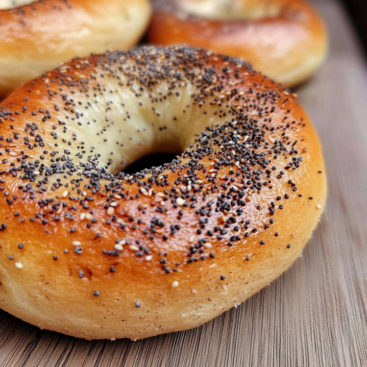 Close-up of a freshly baked homemade poppy seed bagel with a glossy golden-brown crust on a wooden surface.
