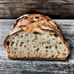 Angeschnittenes Röstkornbrot mit knuspriger Kruste, lockerer Krume und gerösteten Körnern auf einem rustikalen Holztisch.