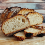 Freshly baked artisan bread with a crispy golden crust and soft open crumb, sliced on a wooden cutting board